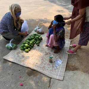 A villager selling her produce on the side of the road receives a mask.