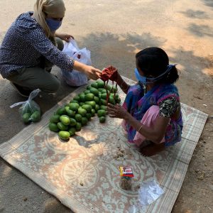 A villager selling her produce on the side of the road receives a mask.